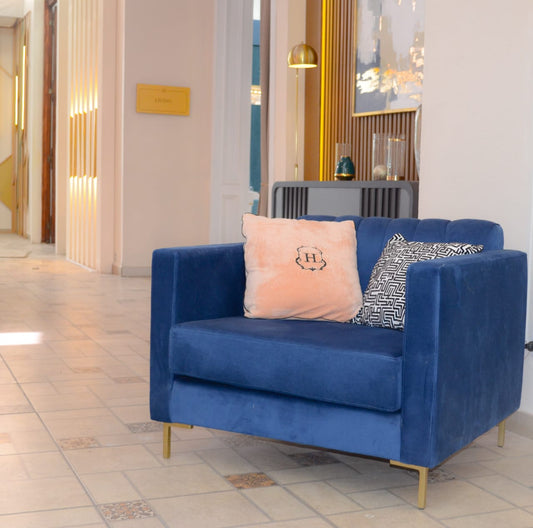 Sillón de un cuerpo tapizado en azul, con respaldo recto acanalado, apoyabrazos rectangulares y base baja con patas doradas.