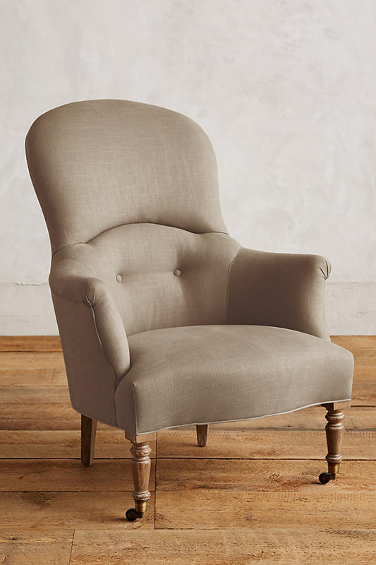 Sillón individual de diseño tradicional en tono beige, con respaldo curvo, apoyabrazos tallados y patas delanteras de madera con ruedas.