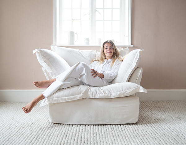 Sillón individual tapizado en blanco, de estilo desenfundable, con asiento y respaldo mullidos, acompañado por dos cojines laterales sueltos que aportan volumen y comodidad.