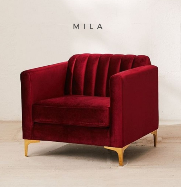 Sillón de un cuerpo tapizado en bordo, con respaldo recto acanalado, apoyabrazos rectangulares y base baja con patas doradas.