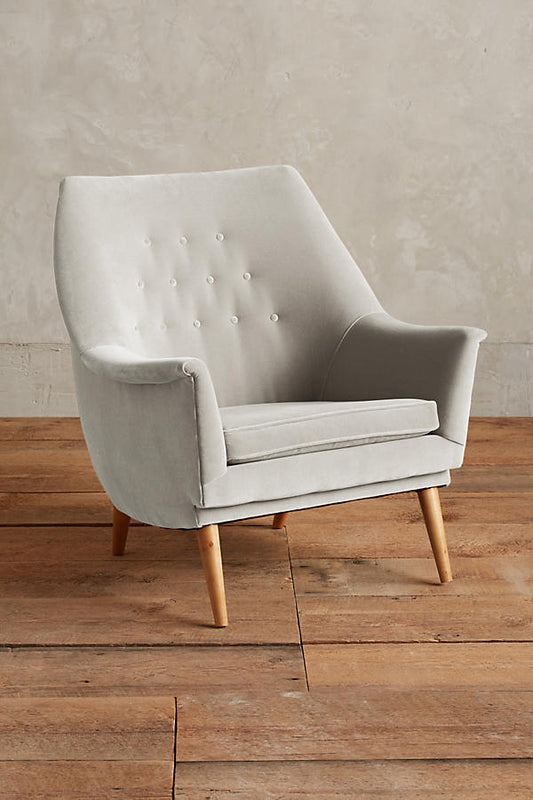 Sillón individual tapizado en terciopelo gris, de diseño retro con respaldo inclinado, asiento acolchado y patas de madera inclinadas estilo escandinavo.