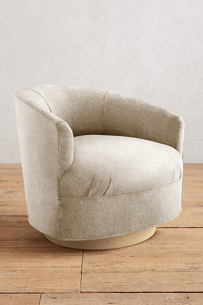 Sillón individual moderno con forma redondeada y base giratoria, tapizado en crema.