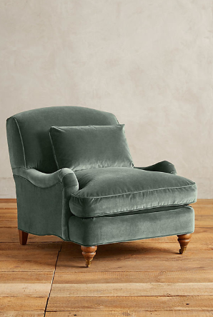Sillón individual tapizado en verde, con cojín lumbar suelto, apoyabrazos curvos, respaldo levemente inclinado y patas torneadas de madera en tono medio.