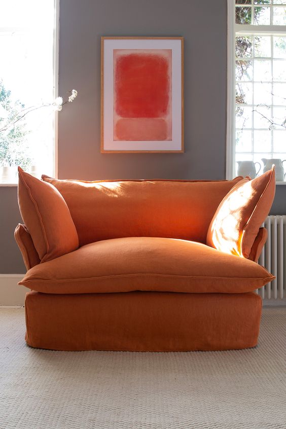 Sillón individual tapizado en naranja, de estilo desenfundable, con asiento y respaldo mullidos, acompañado por dos cojines laterales sueltos que aportan volumen y comodidad.