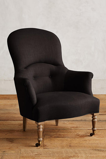 Sillón individual de diseño tradicional en tono negro, con respaldo curvo, apoyabrazos tallados y patas delanteras de madera con ruedas.