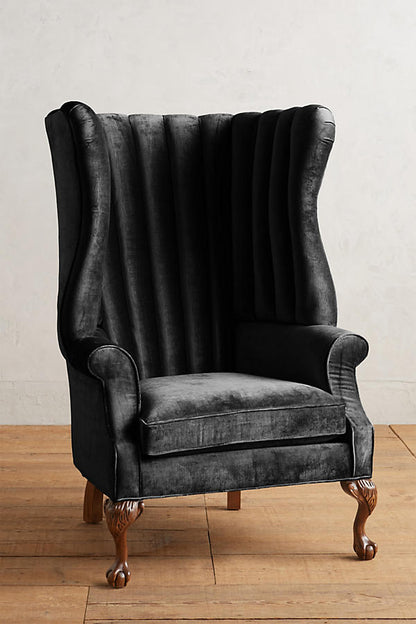 Sillón individual tapizado en negro, con respaldo alto acanalado de líneas verticales, brazos curvos y patas delanteras torneadas con ruedas pequeñas.