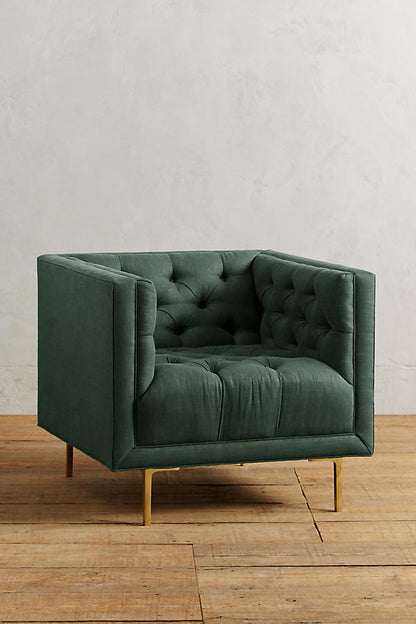 Sillón individual tapizado en verde, de forma cúbica con respaldo y brazos rectos, capitoné de botones en todo el interior y patas delgadas de madera.