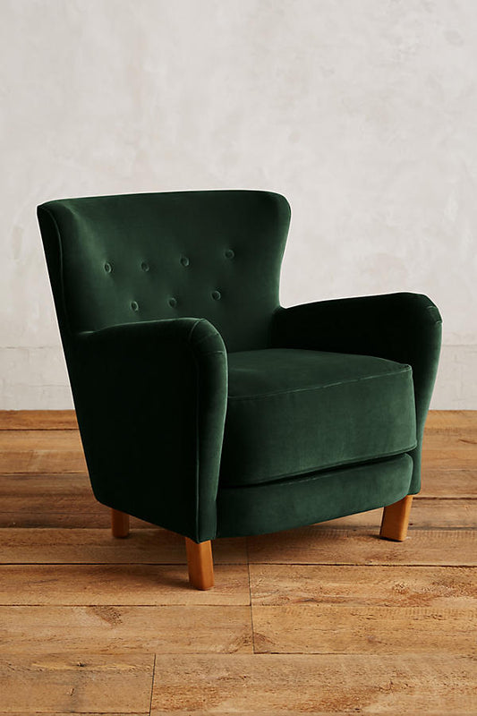 Sillón individual tapizado en verde, con respaldo suavemente inclinado y capitoné de botones, brazos redondeados y patas cortas de madera.