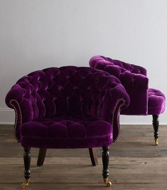 Sillón individual tapizado en violeta, con respaldo y asiento redondeados totalmente capitoné, brazos curvos integrados y patas de madera claras.