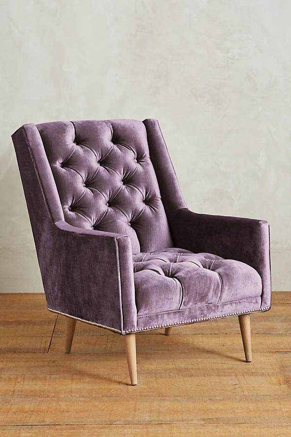 Sillón individual tapizado en violeta, con respaldo capitoné de botones, brazos rectos y patas de madera inclinadas.