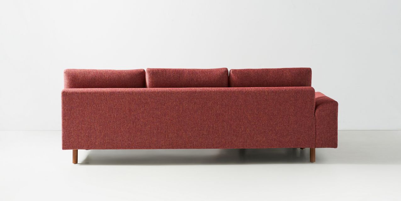 Sillón esquinero moderno en pana rosa oscuro, respaldo alto y estructura sólida con patas de madera natural.