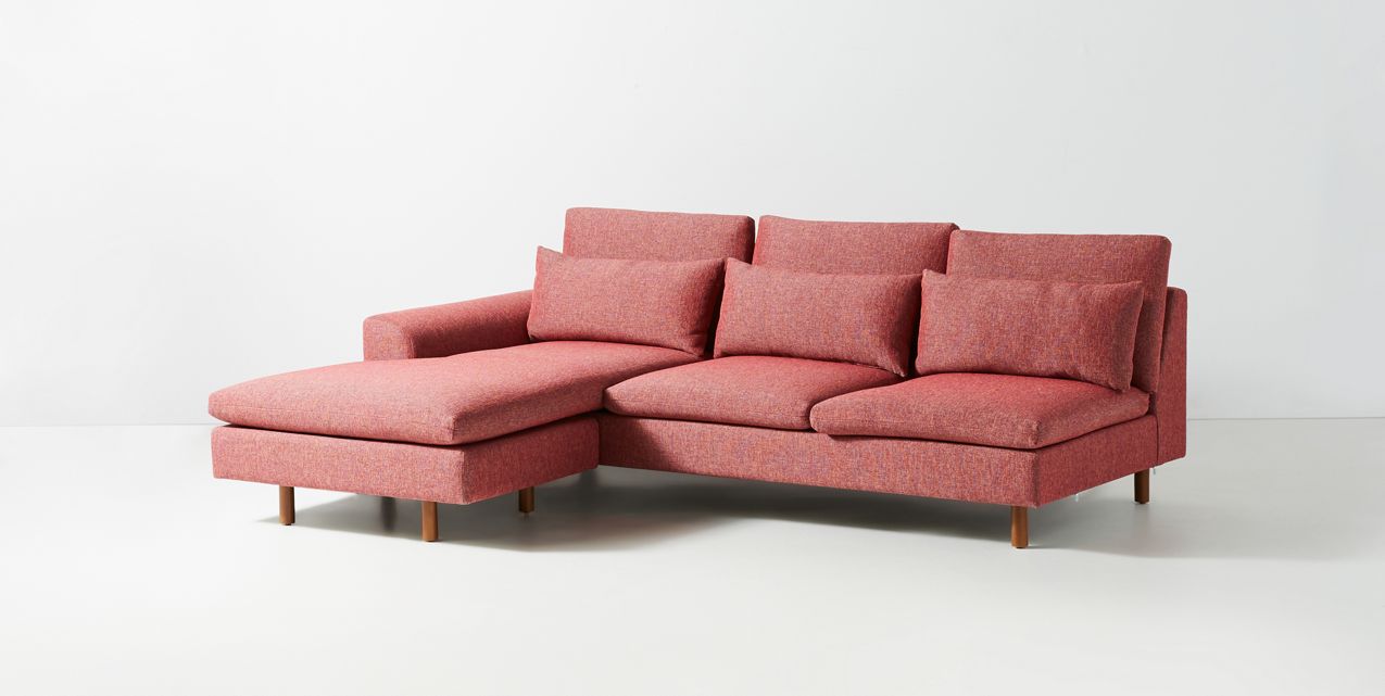 Sillón esquinero moderno en pana rosa oscuro, respaldo alto y estructura sólida con patas de madera natural.