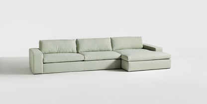 Sillón esquinero tapizado en gris, diseño lineal con base baja y almohadones grandes. Estética minimalista y fresca.