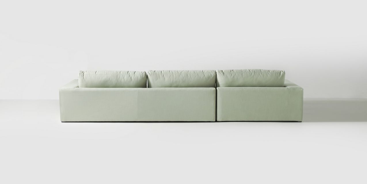 Sillón esquinero tapizado en gris, diseño lineal con base baja y almohadones grandes. Estética minimalista y fresca.