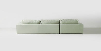 Sillón esquinero tapizado en gris, diseño lineal con base baja y almohadones grandes. Estética minimalista y fresca.