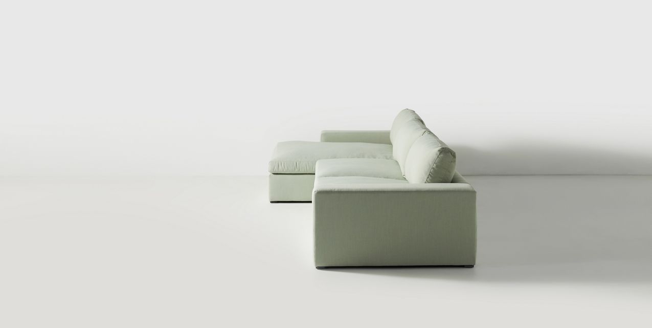 Sillón esquinero tapizado en gris, diseño lineal con base baja y almohadones grandes. Estética minimalista y fresca.