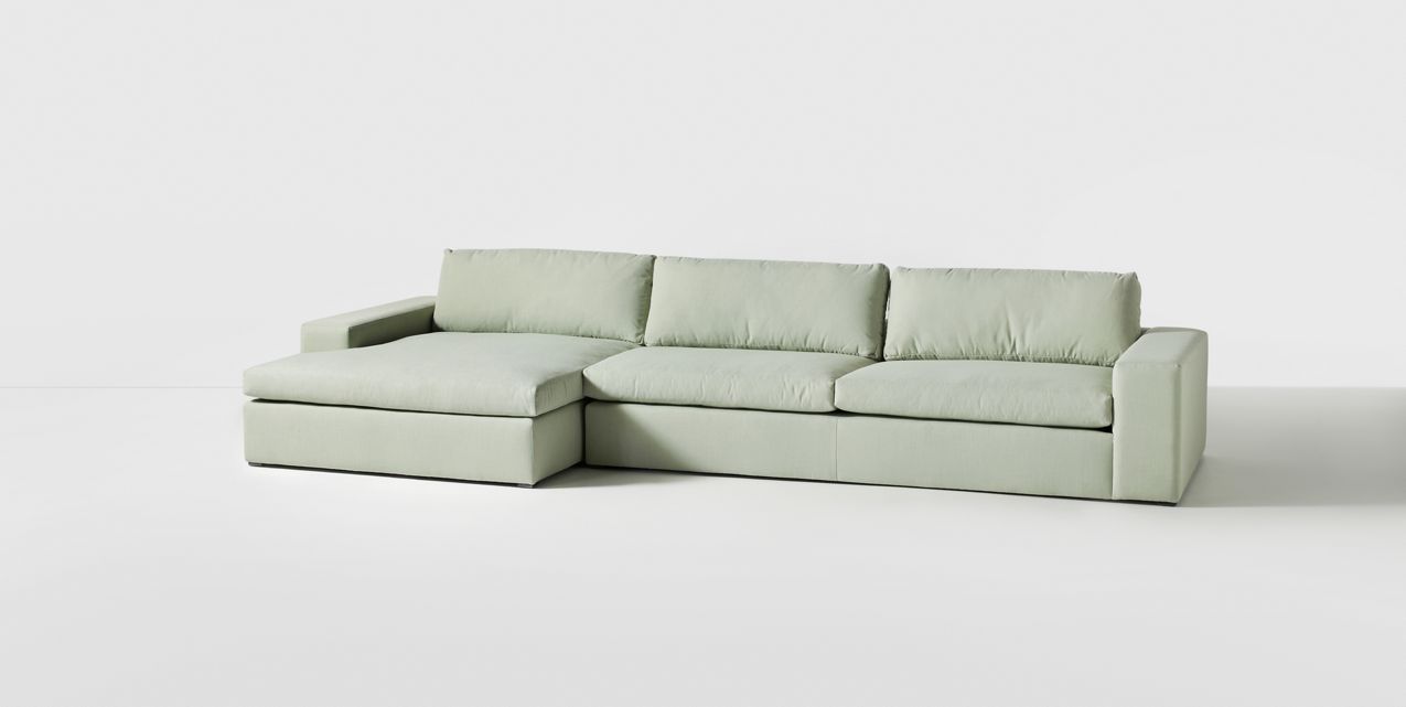 Sillón esquinero tapizado en gris, diseño lineal con base baja y almohadones grandes. Estética minimalista y fresca.