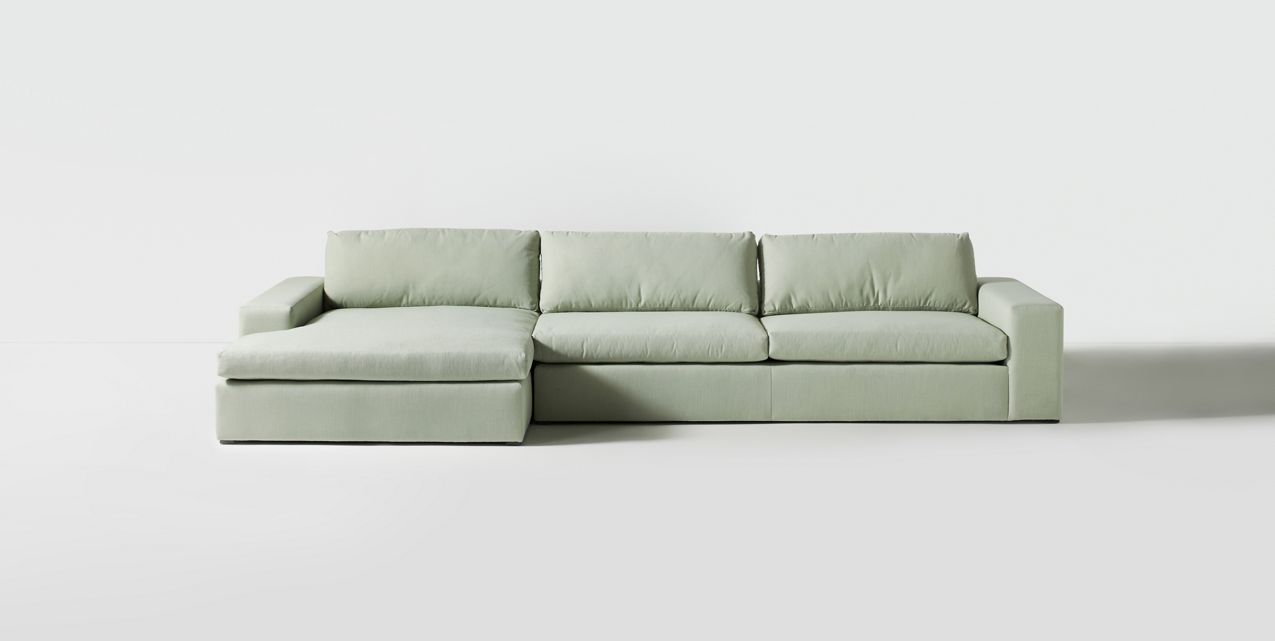 Sillón esquinero tapizado en gris, diseño lineal con base baja y almohadones grandes. Estética minimalista y fresca.