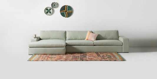 Sillón esquinero tapizado en gris, diseño lineal con base baja y almohadones grandes. Estética minimalista y fresca.