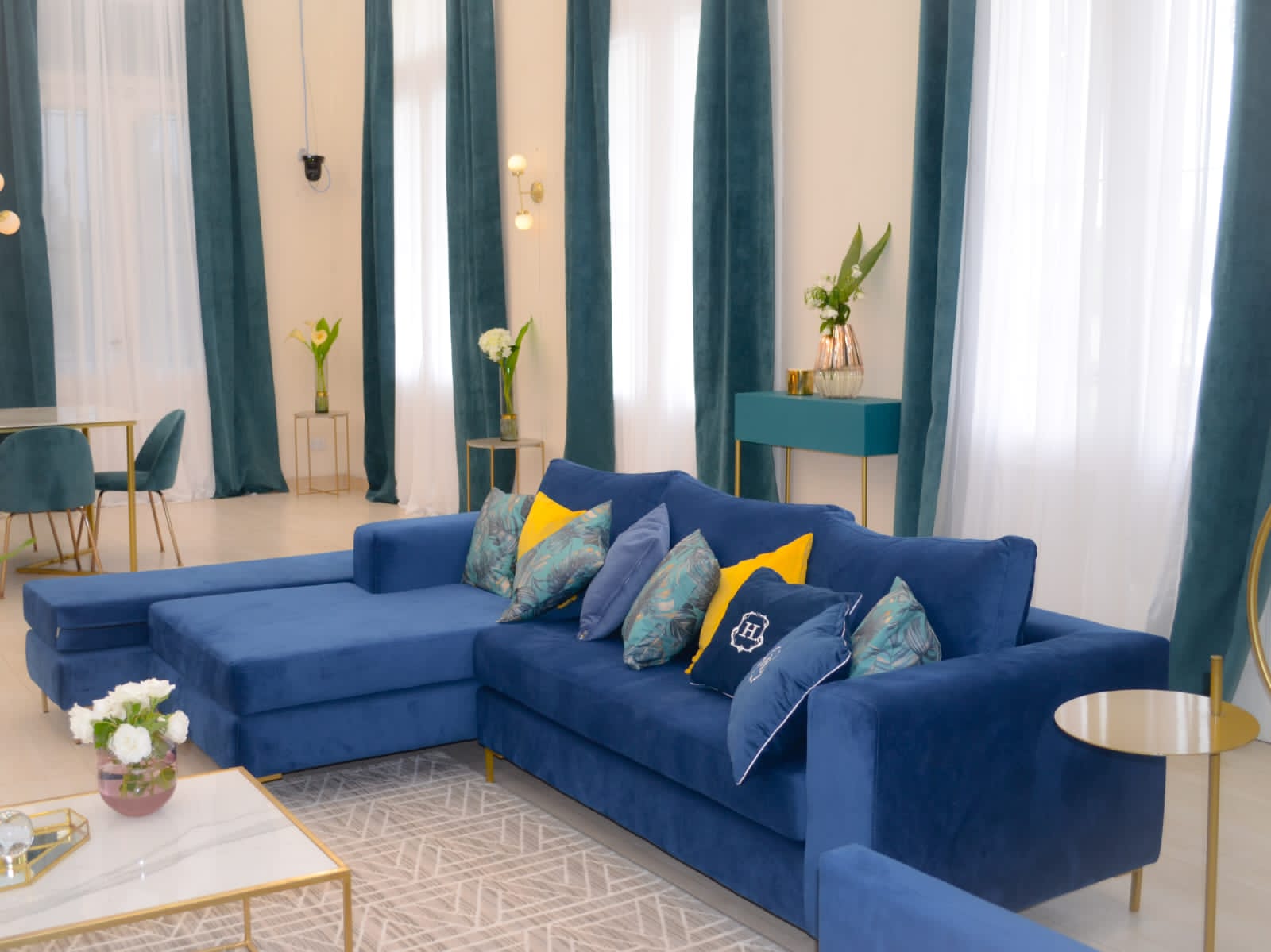 Sillón esquinero moderno en azul con patas doradas, líneas limpias y almohadones sueltos. Estilo nórdico con toque glam.