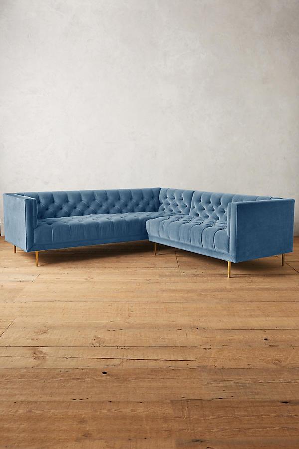 Sillón esquinero clásico en celeste con respaldo capitoné profundo, apoyabrazos rectos y patas finas de madera. Diseño elegante y sofisticado.