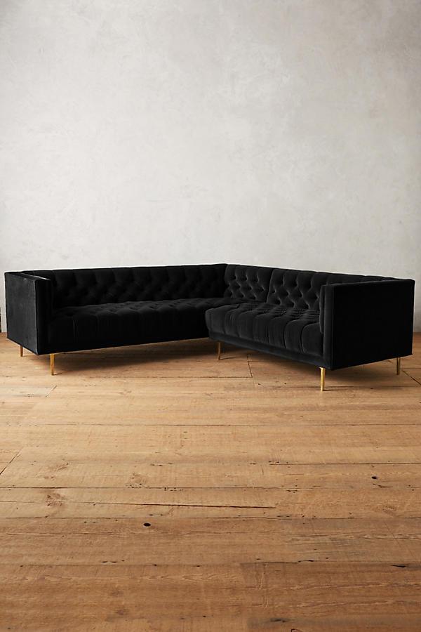 Sillón esquinero clásico en negro con respaldo capitoné profundo, apoyabrazos rectos y patas finas de madera. Diseño elegante y sofisticado.