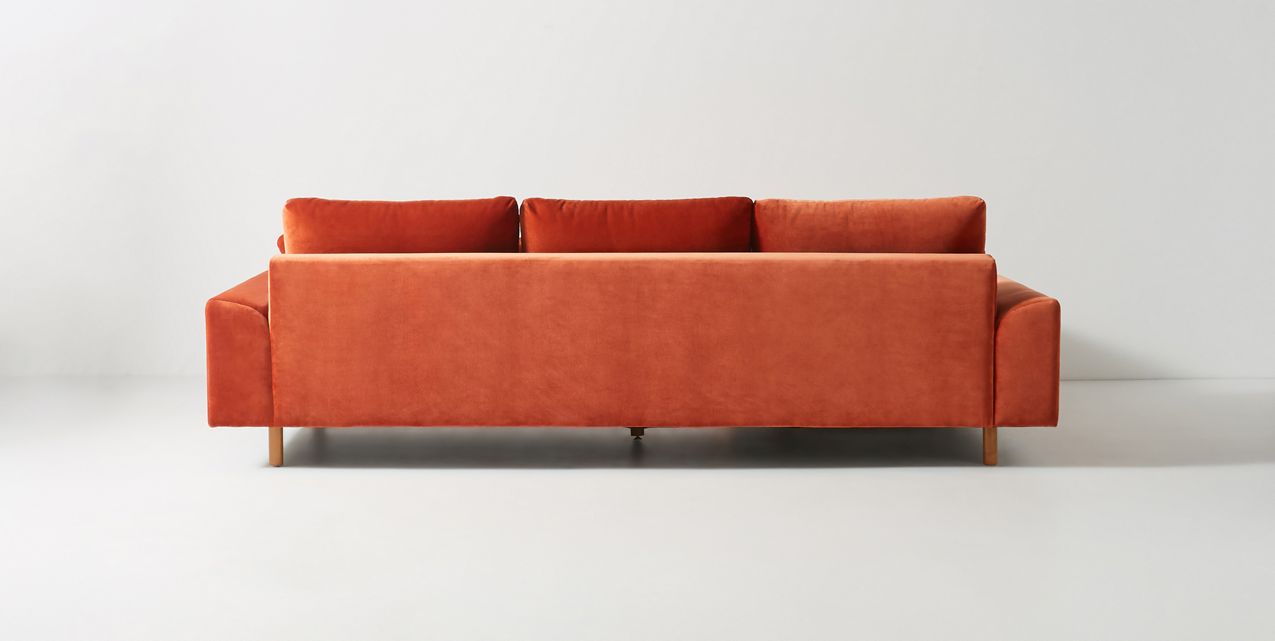 Sillón esquinero en tono rojo con líneas rectas, patas de madera claras y apoyabrazos rectangulares. Ideal para espacios cálidos.
