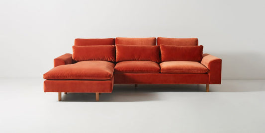 Sillón esquinero en tono rojo con líneas rectas, patas de madera claras y apoyabrazos rectangulares. Ideal para espacios cálidos.