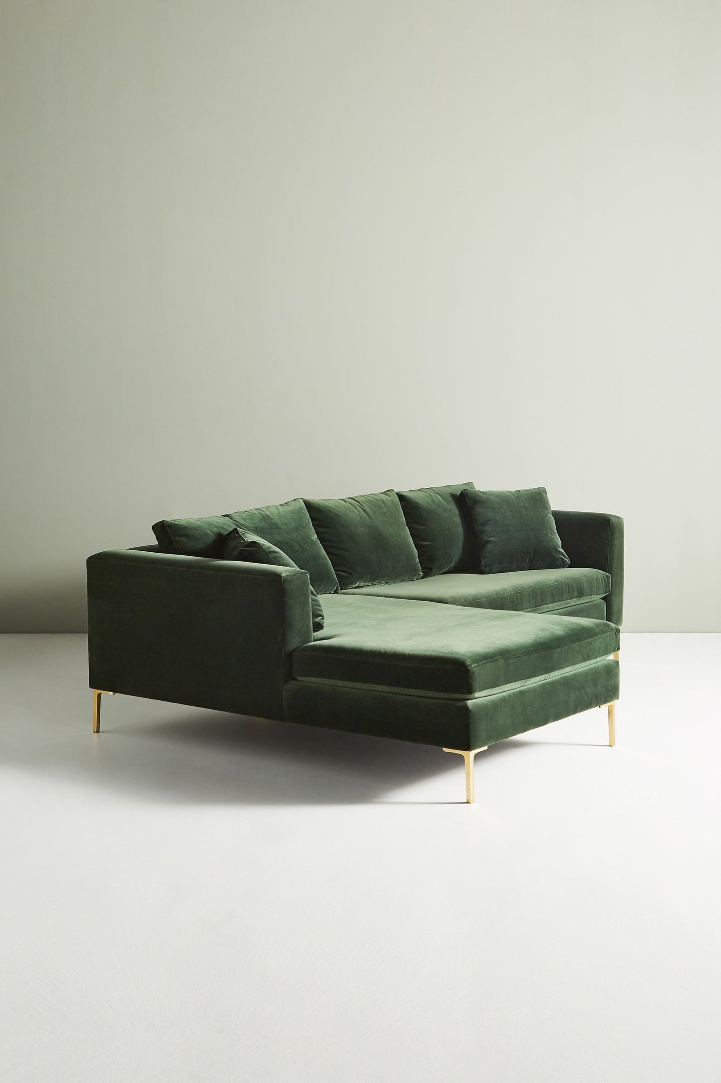 Sillón esquinero moderno en verde con patas doradas, líneas limpias y almohadones sueltos. Estilo nórdico con toque glam.