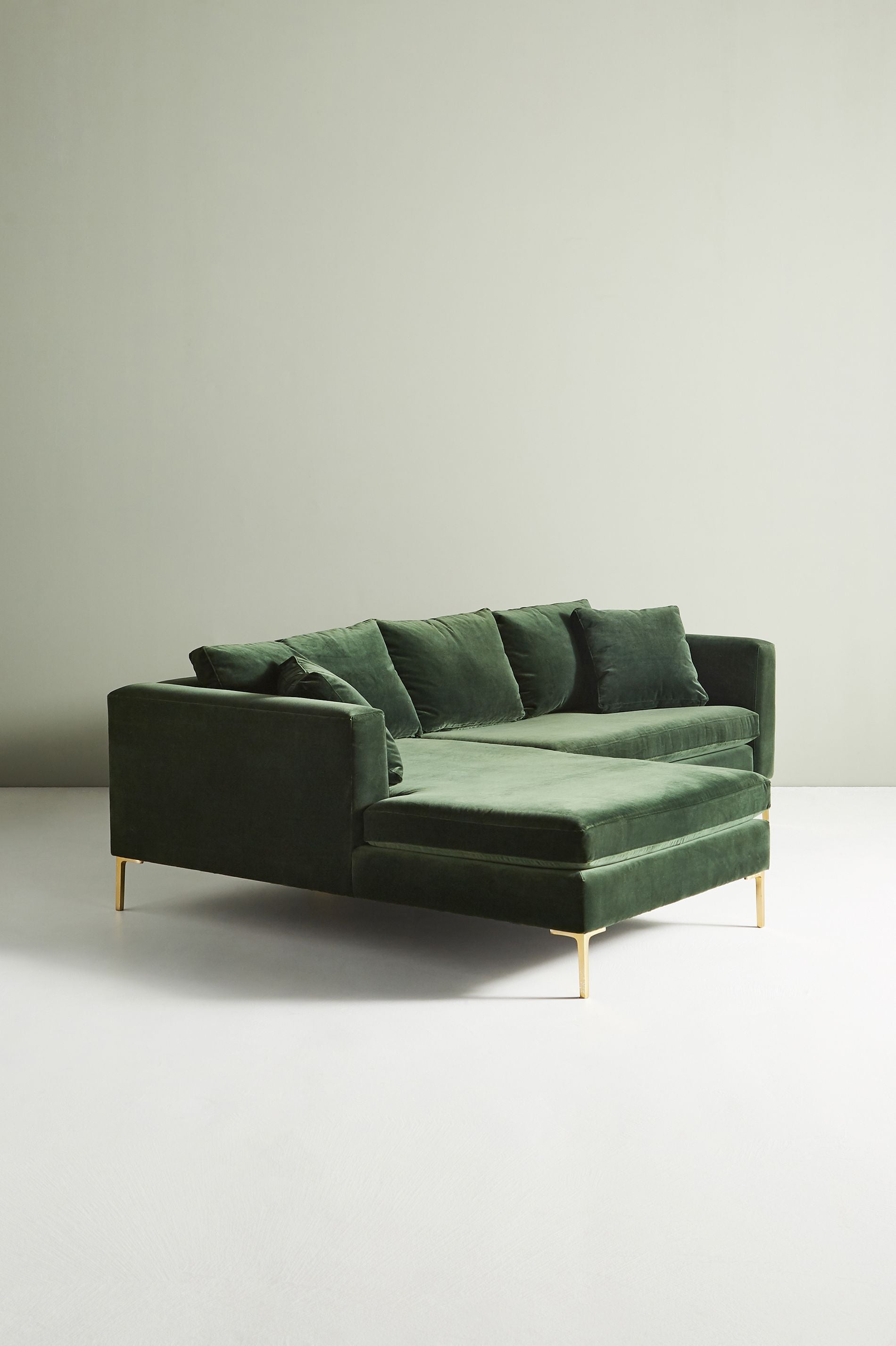 Sillón esquinero moderno en verde con patas doradas, líneas limpias y almohadones sueltos. Estilo nórdico con toque glam.