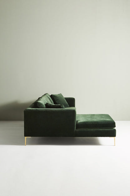 Sillón esquinero moderno en verde con patas doradas, líneas limpias y almohadones sueltos. Estilo nórdico con toque glam.