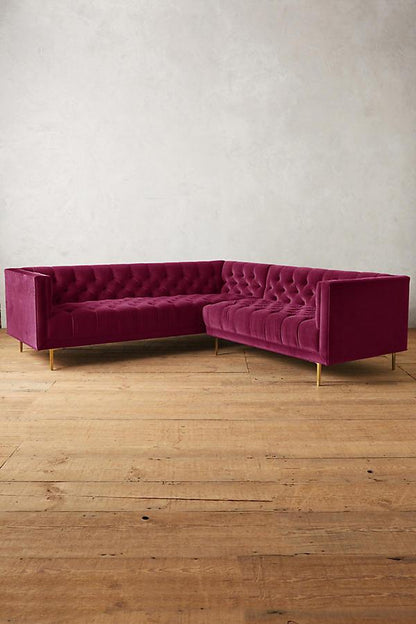 Sillón esquinero clásico en violeta con respaldo capitoné profundo, apoyabrazos rectos y patas finas de madera. Diseño elegante y sofisticado.