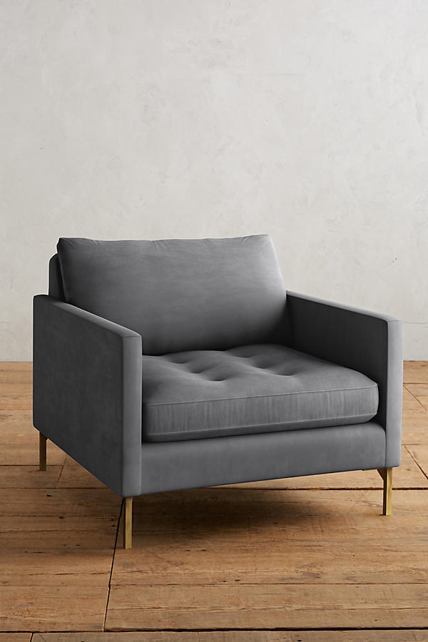 Sillón individual moderno en color gris con respaldo y asiento acolchados, apoyabrazos rectos y patas metálicas finas en dorado, sobre fondo blanco.