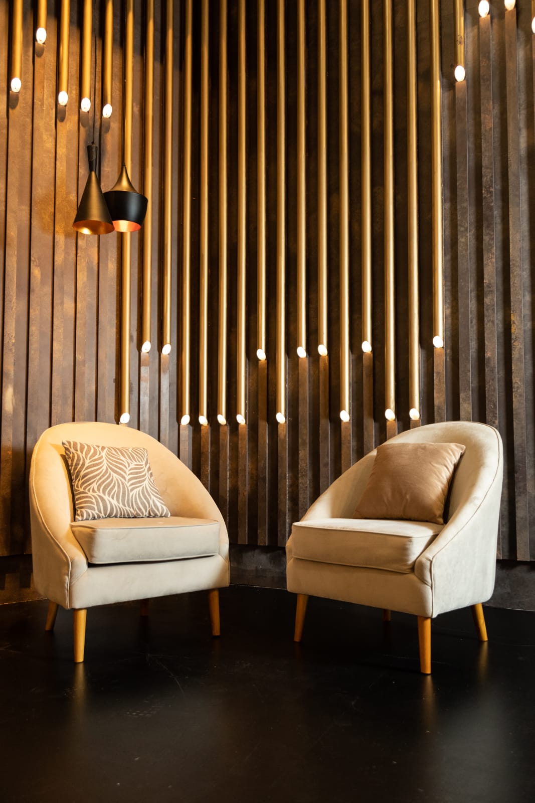 Par de sillones individuales tapizados en tono beige con patas de madera, de diseño moderno y respaldo curvo, decorados con almohadones a tono, ideales para un ambiente elegante y acogedor
