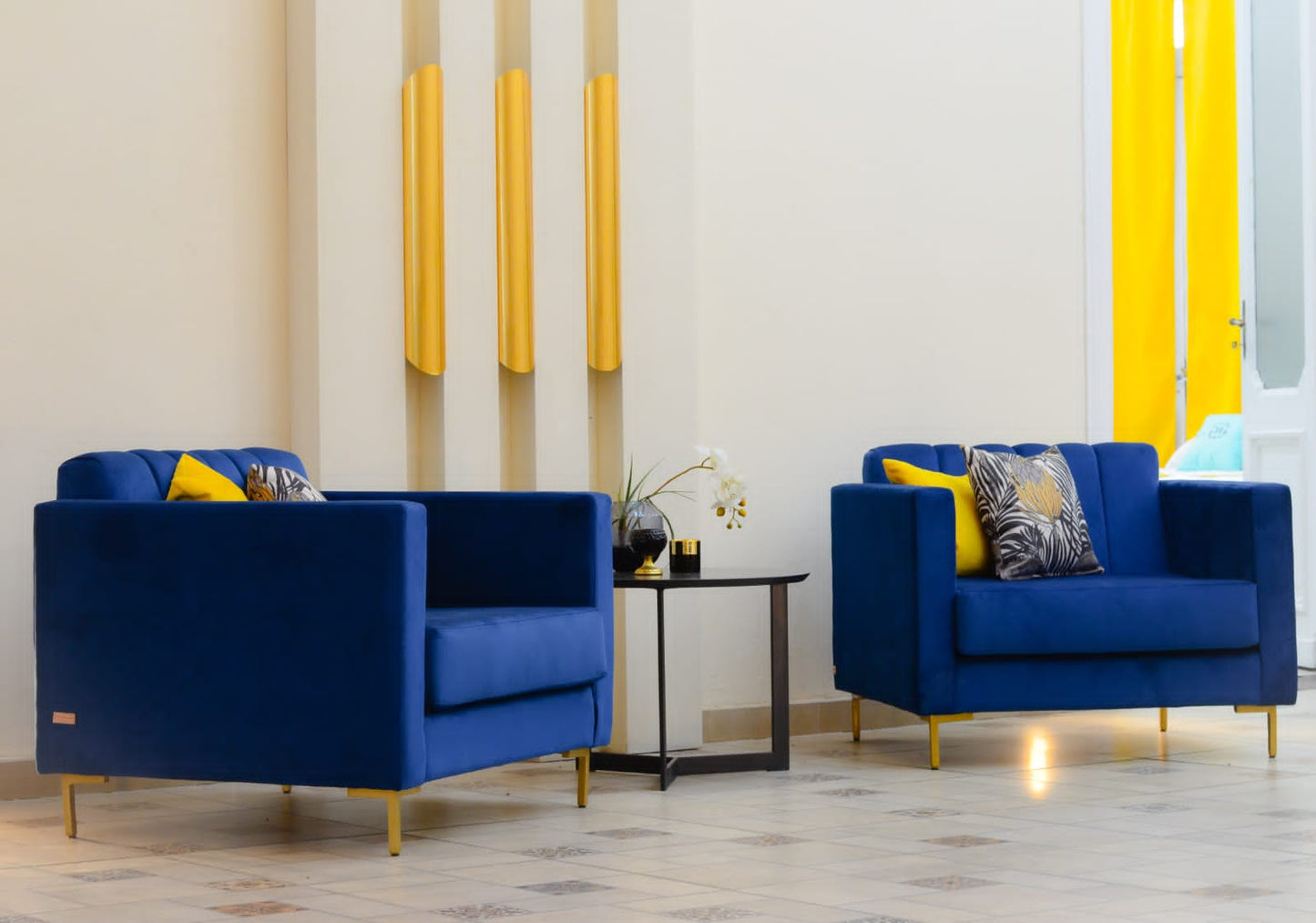Sillón de un cuerpo tapizado en azul, con respaldo recto acanalado, apoyabrazos rectangulares y base baja con patas doradas.
