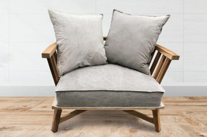 Sillón individual de estructura de madera clara con brazos y respaldo de listones, cojines grises sueltos en asiento y respaldo, de diseño minimalista y estilo escandinavo.