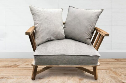 Sillón individual de estructura de madera clara con brazos y respaldo de listones, cojines grises sueltos en asiento y respaldo, de diseño minimalista y estilo escandinavo.