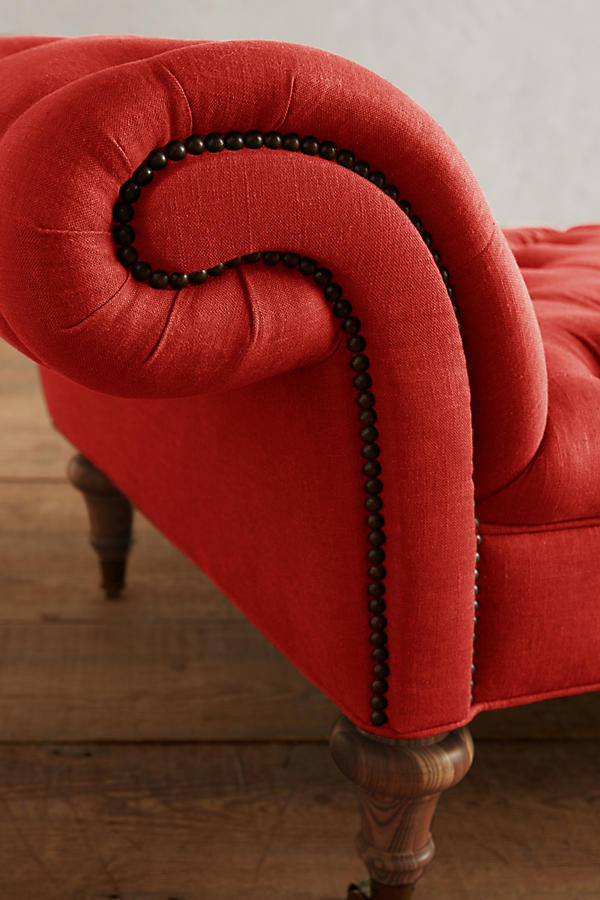 Detalle del brazo enrollado con tachas de la Banqueta Chesterfield roja y su pata torneada de madera