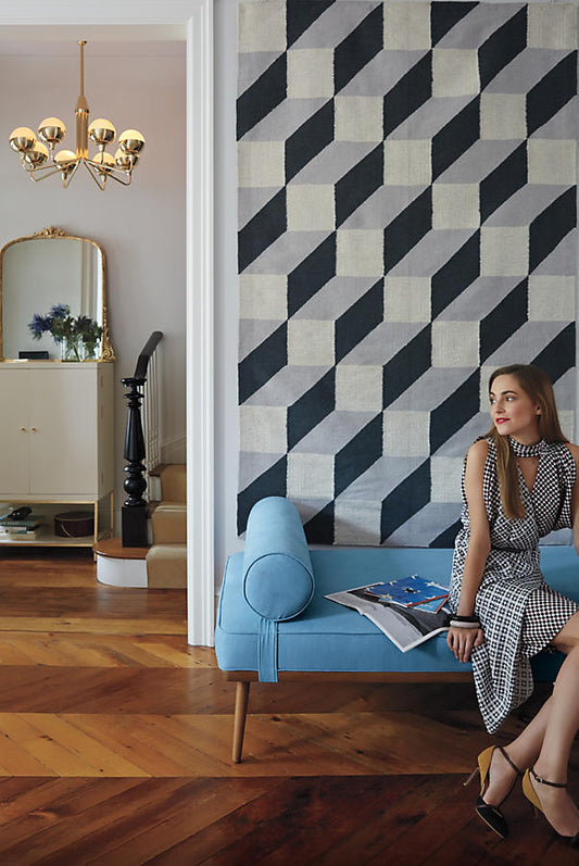 Mujer sentada en una Banqueta Escandinava celeste, junto a una pared de azulejos geométricos