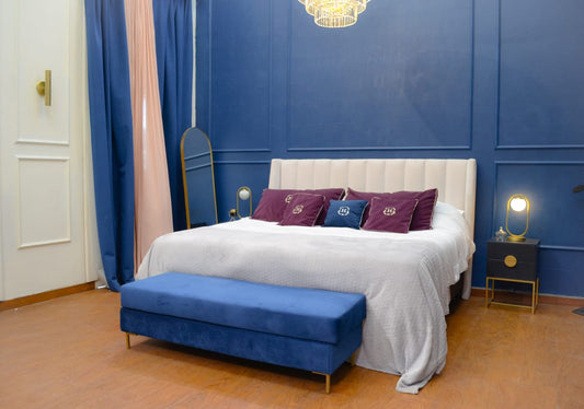 Banqueta Unique azul al pie de la cama, con el Respaldo Alpes, en la suite de El Hotel de los Famosos 2023