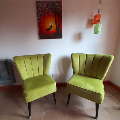 Dos butacas verde lima de respaldo acanalado y patas de madera oscura, debajo de un cuadro de un atardecer en la casa de Carla