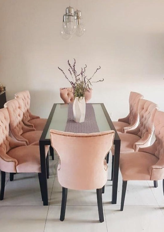 Comedor de Guillermina con Sillas Charis en terciopelo rosa con capitoné y tachas, alrededor de una mesa de vidrio