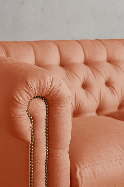 Detalle del brazo enrollado con tachas y el capitoné del Sillón esquinero Chesterfield en rosa salmón