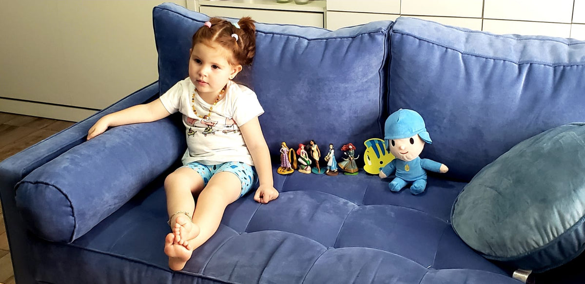 Hija de Romina sentada en el Esquinero Bambú azul, con almohadón cilíndrico en el brazo y asiento capitoné