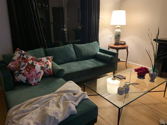 Esquinero Bambú verde con chaise longue, almohadones floreados, almohadones cilíndricos y manta clara, frente a una mesa ratona de vidrio en el living de Patri