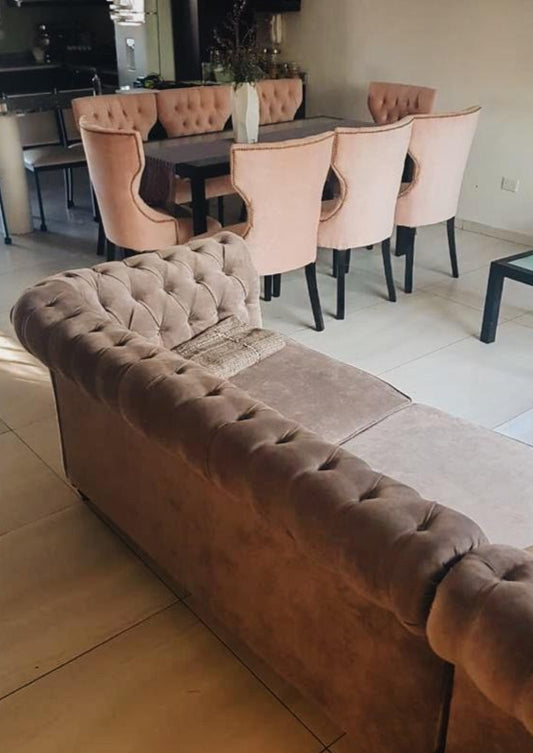 Esquinero Chesterfield en primer plano y comedor con sillas rosas con capitoné de fondo, en la casa de Guillermina