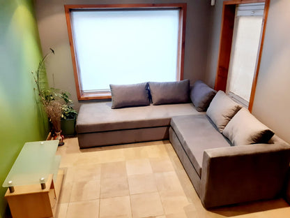 Esquinero Cúrcuma gris con base tapizada sin patas a la vista y almohadones de respaldo sueltos, junto a una ventana con marco de madera en el living de Carla