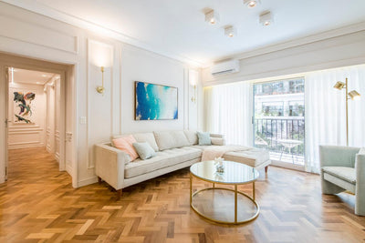 Sofá esquinero tapizado en tono beige claro, con almohadones a juego, ubicado en un living luminoso de estilo moderno.