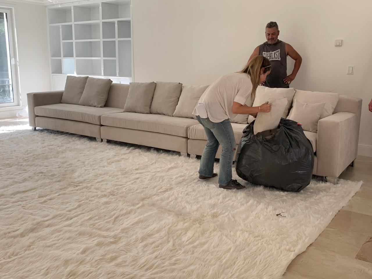 Amplio living con sillones tapizados en tono beige, dos butacas clásicas al frente y una gran alfombra blanca de pelo largo en el centro, acompañado por una chimenea y ventanales que aportan luz natural al espacio.