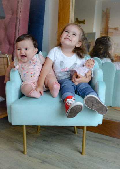 Una nena y una bebé sentadas juntas en un Mini Angie celeste con patas doradas